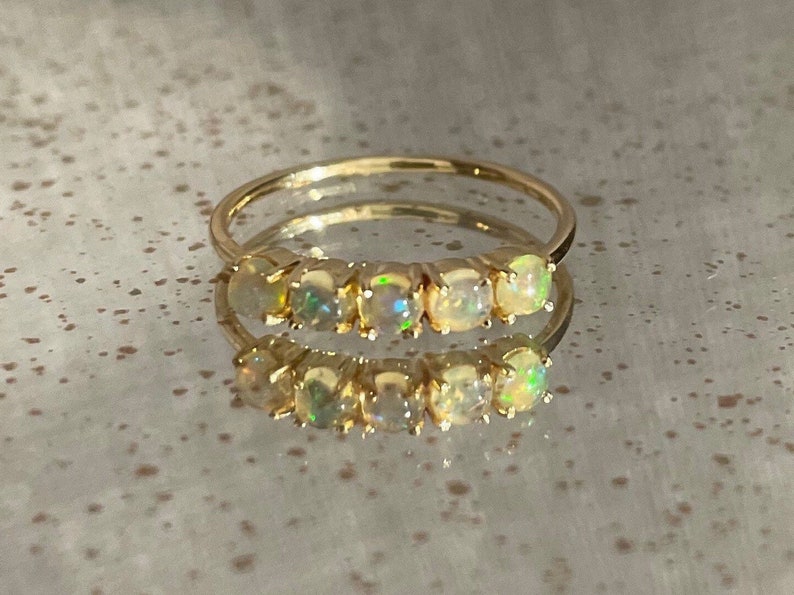 May include: A gold band ring with five round opal gemstones set in a row. The opals are iridescent and have a milky white color.