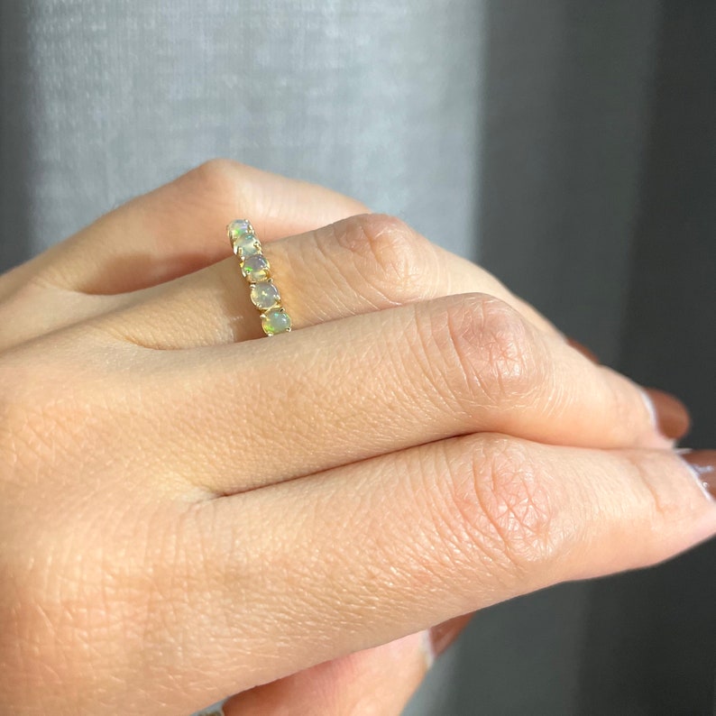 May include: A gold band ring with a row of round, white opals.
