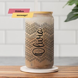 May include: A clear glass tumbler with a bamboo lid, filled with a beverage. The tumbler is decorated with a black pattern and the name "Olivia" in a script font. The text "Hidden message!" is displayed on a pink and yellow banner.