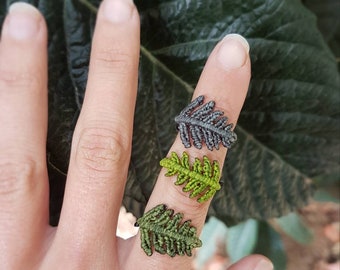 Könnte beinhalten: Drei fर्न-förmige Ringe, einer dunkelgrau, einer hellgrün und einer dunkelgrün, an einem Finger getragen.