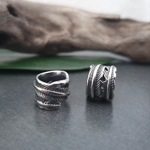 May include: Two silver ear cuffs with a feather design. The cuffs are made of metal and have a textured finish.