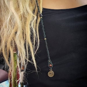 Könnte beinhalten: Nahaufnahme von blonden Haaren einer Person mit einem grünen und braunen Perlenhaarband mit einem Spiral-Anhänger.