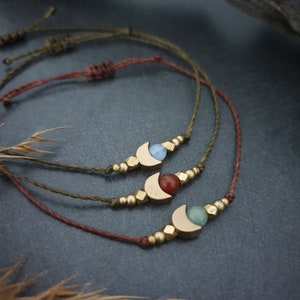 May include: Three bracelets featuring a crescent moon charm and a gemstone bead. The bracelets are crafted with brown and green cord and gold beads. The gemstones are blue, red, and green.