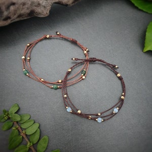 Può includere: Due braccialetti con cordoncino marrone e perline dorate. Un braccialetto ha perline verdi e l'altro ha perline blu chiaro.