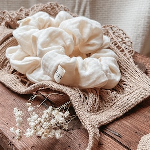 Könnte beinhalten: Ein weißer Stoff-Haargummi mit einem kleinen "en"-Etikett, der auf einer braunen gehäkelten Tasche und einer Holzoberfläche liegt.