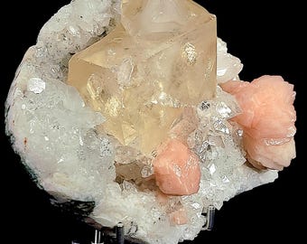 May include: A close-up of a natural crystal cluster. The image shows a large, pale-yellow calcite crystal formation, complemented by clear quartz and peach-coloured stilbite crystals, forming a unique mineral specimen.