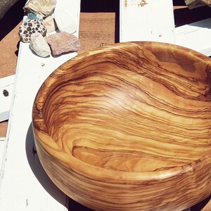 Large salad bowl or round fruit bowl made of olive wood. Salad bowl with drawings of highly veined wood. Medium brown colour. Top side view of the salad bowl.