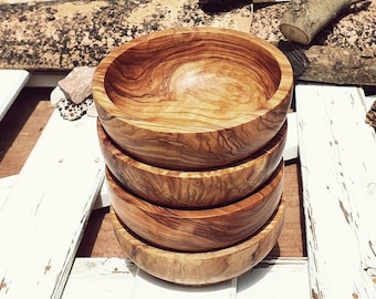 May include: A stack of four wooden bowls made from olive wood. The bowls are nested inside each other and have a natural wood grain pattern. The bowls are sitting on a white wooden surface.