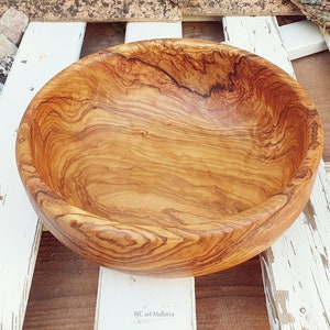 Large salad bowl or round fruit bowl made of olive wood. Salad bowl with drawings of highly veined wood. Medium brown colour. Top side view of the salad bowl.