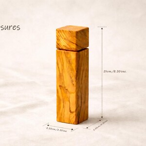 Op de afbeelding: Een houten zout- of pepermolen met een vierkante bovenkant en een rechthoekig lichaam. De molen is 21 cm hoog en 5,50 cm breed. Het hout heeft een natuurlijke, lichtbruine kleur met zichtbare nerf.
