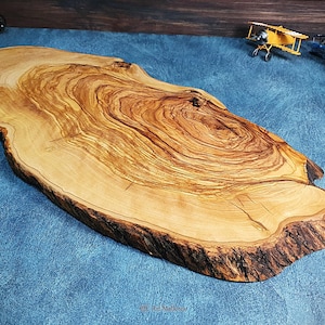 May include: A large, oval-shaped wooden serving board made from olive wood. The board has a natural, rustic finish with a beautiful grain pattern. It is perfect for serving cheese, charcuterie, or other appetizers.