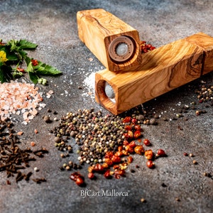 Olive wood pepper shaker on a table with design and square shape. Side view, with peppers and salt on the table, different pepper shakers on the table.