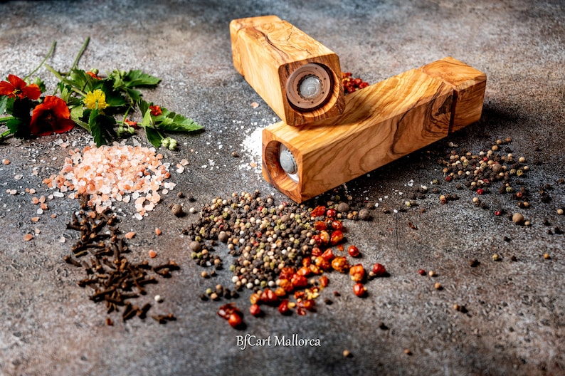 Olive wood pepper shaker on a table with design and square shape. Side view, with peppers and salt on the table, different pepper shakers on the table.