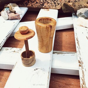 May include: Two wooden containers with lids, one tall and one short, made from olive wood with a natural wood grain pattern. The containers are sitting on a white wooden surface.
