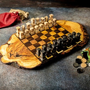 May include: A wooden chess set with light and dark brown pieces on a natural olive wood board. The board is a slice of a tree trunk with a natural edge. The pieces are arranged in a starting position. There are two small bags with game pieces next to the board.