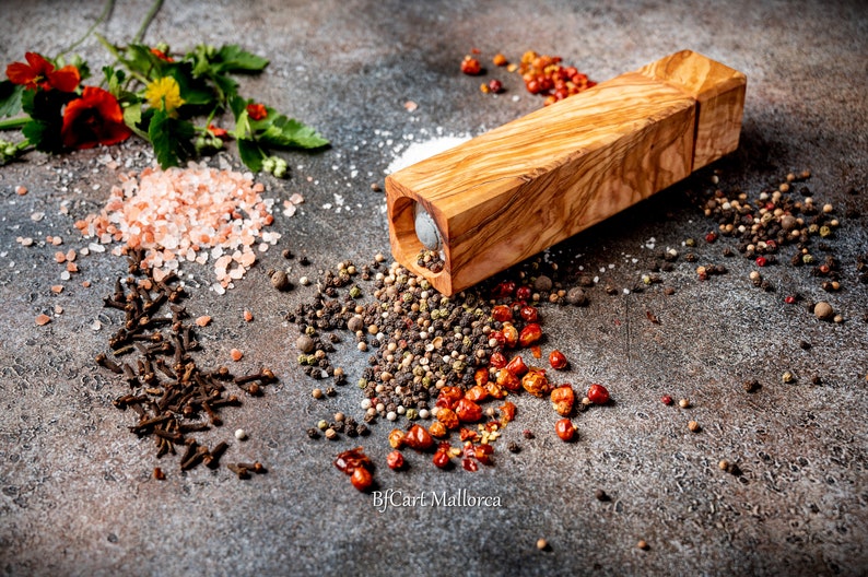 Pode incluir: Um moinho de pimenta de madeira de cor castanho claro com um padr&atilde;o de gr&atilde;o de madeira natural. O moinho &eacute; rodeado por v&aacute;rias especiarias, incluindo sal rosa do Himalaia, gr&atilde;os de pimenta preta, gr&atilde;os de pimenta branca, cravos e flocos de pimenta vermelha.