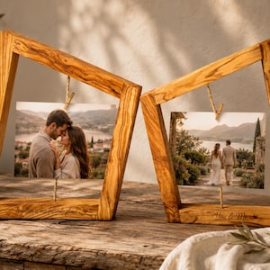 May include: Two trapezoidal wooden photo frames made of light brown wood with a distinct grain pattern. Each frame holds a rectangular photograph suspended by a small clip. The left frame is engraved with "Together is my favorite place" and the right frame with "You & Me".