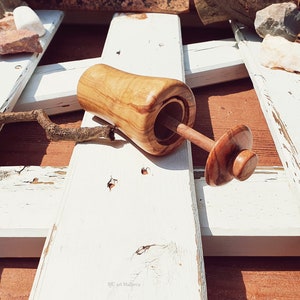 May include: A wooden salt and pepper shaker set with a natural wood finish. The shaker is open and the lid is off, revealing the salt or pepper inside. The set is sitting on a white wooden surface.