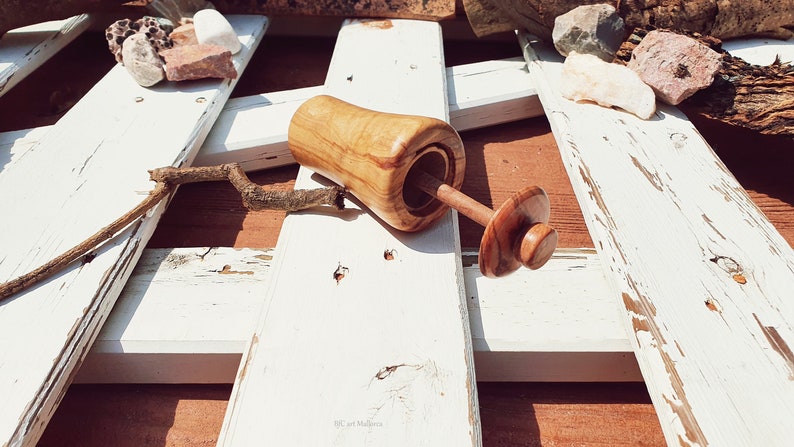 May include: A wooden salt and pepper shaker set with a natural wood finish. The shaker is open and the lid is off, revealing the salt or pepper inside. The set is sitting on a white wooden surface.
