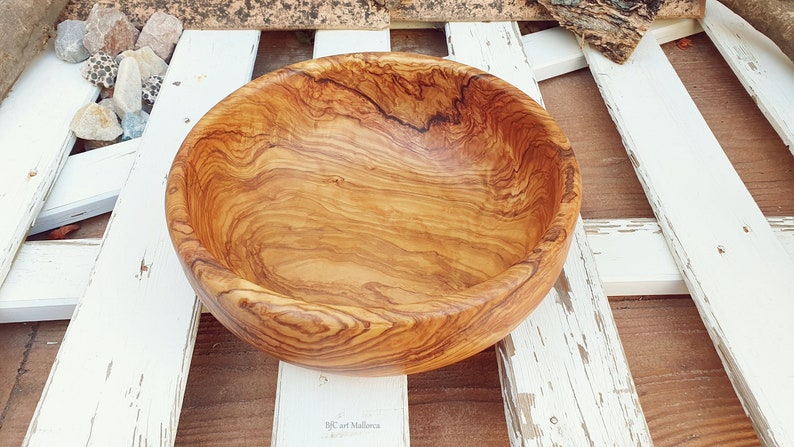 Large salad bowl or round fruit bowl made of olive wood. Salad bowl with drawings of highly veined wood. Medium brown colour. Top side view of the salad bowl.