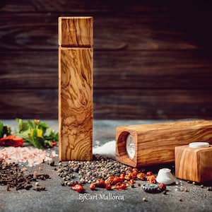 Pode incluir: Dois moinhos de sal e pimenta de madeira com acabamento de gr&atilde;o de madeira natural. Os moinhos s&atilde;o feitos de madeira de oliveira e t&ecirc;m um design simples e elegante. Os moinhos s&atilde;o rodeados por v&aacute;rias especiarias, incluindo sal rosa do Himalaia, gr&atilde;os de pimenta preta e cravos.