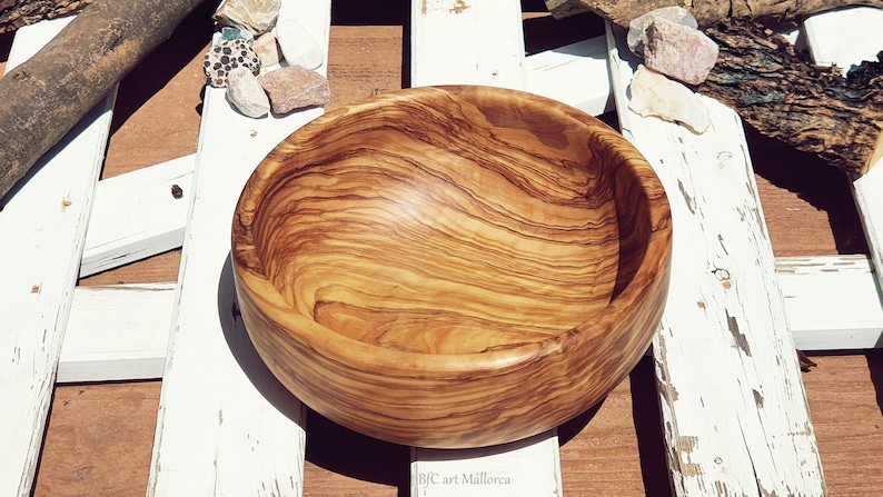 Large salad bowl or round fruit bowl made of olive wood. Salad bowl with drawings of highly veined wood. Medium brown colour. Top side view of the salad bowl.