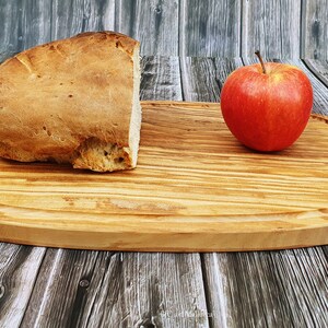 Op de afbeelding: Een houten snijplank met een afgeronde rand, met een brood en een rode appel.