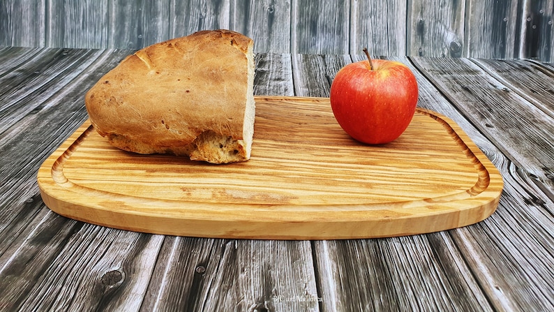 Op de afbeelding: Een houten snijplank met een afgeronde rand, met een brood en een rode appel.