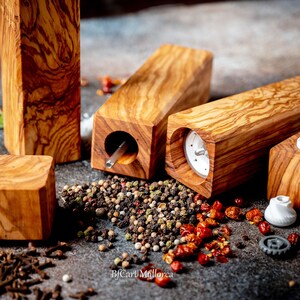 Olive wood pepper shaker on table with design and square shape. Side view, with peppers and salt on the table, different pepper shakers on the table. Disassembled pepper shaker shows the ceramic grinding mechanism.