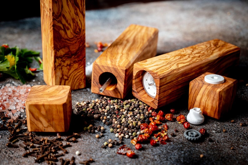Olive wood pepper shaker on table with design and square shape. Side view, with peppers and salt on the table, different pepper shakers on the table. Disassembled pepper shaker shows the ceramic grinding mechanism.
