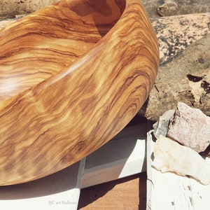 Large salad bowl or round fruit bowl made of olive wood. Salad bowl with highly grained wood drawings. Medium brown colour. Top side view of the salad bowl.