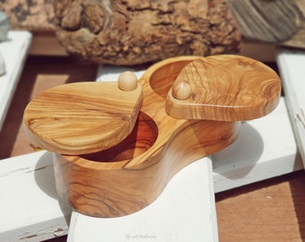 May include: A wooden salt and pepper shaker set with two compartments. The shakers are made of olive wood and have a natural finish. The shakers have a unique, organic shape and are perfect for adding a touch of rustic charm to any kitchen.