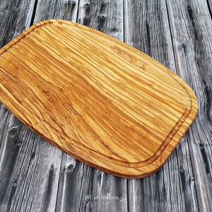 Op de afbeelding: Een groot, ovaal houten snijplank met een natuurlijke houtnerf afwerking. Het plank heeft een verhoogde rand rondom de omtrek.