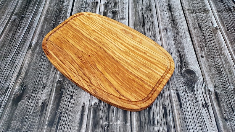 Op de afbeelding: Een groot, ovaal houten snijplank met een natuurlijke houtnerf afwerking. Het plank heeft een verhoogde rand rondom de omtrek.