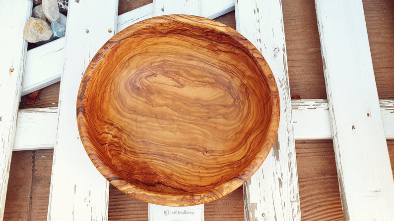 Large salad bowl or round fruit bowl made of olive wood. Salad bowl with drawings of highly veined wood. Medium brown colour. Top side view of the salad bowl. Top views