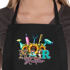 May include: Black apron with a graphic of hair styling tools and the text "Hair Hustler".