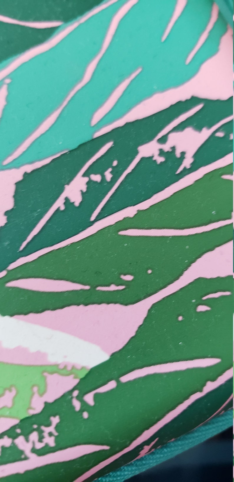 May include: Abstract design featuring overlapping leaf shapes in green, teal, and pink. The design has a textured appearance with a pattern of pink lines and shapes on a green background. The image is a close-up.