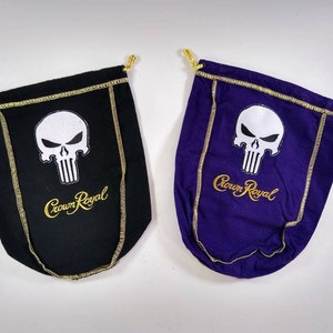 May include: Two Crown Royal bags, one black and one purple, each featuring a white skull graphic and gold embroidered text. The bags have gold trim and drawstrings.