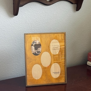 May include: A rectangular picture frame with a metallic gold finish and an embossed floral pattern. The frame features five oval-shaped openings for photographs, with the text 5 Opening Memory Collection and the Intervall brand logo printed on the mat.