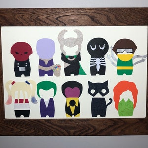 May include: A framed artwork featuring colorful paper cutouts of comic book characters. The characters include Red Skull, Thanos, Loki, Venom, Doctor Octopus, Harley Quinn, Joker, and others. The frame is made of dark brown wood.