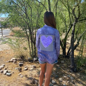 May include: A purple tie-dye button-up shirt with a large purple heart on the back. The heart has a white outline and the word "Love" written inside.