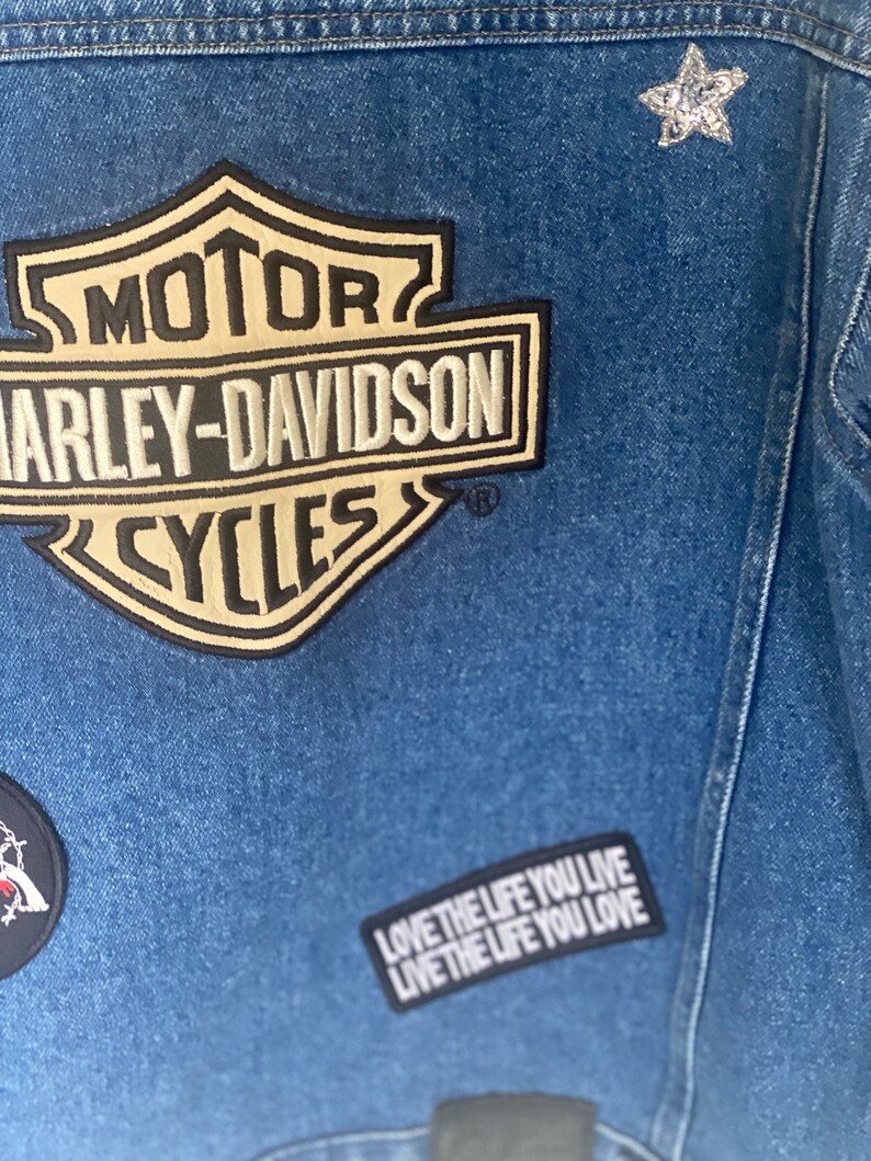Peut inclure: Une veste en jean bleue avec un patch logo Harley-Davidson, une &eacute;toile argent&eacute;e et un patch noir et blanc qui dit "Love the life you live".