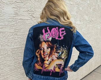 Puede incluir: Una chaqueta vaquera azul con un parche negro en la espalda. El parche presenta una foto de una mujer con una corona y el texto "HOLE Live Through This".