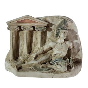 May include: A white plaster relief sculpture depicting a reclining warrior in a helmet, with a partially visible temple behind him. The sculpture has a textured surface and is set against a white background.