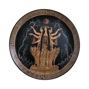 Pode incluir: Um prato de cerâmica preto e dourado com uma cena mitológica grega que retrata uma deusa de três cabeças com lobos de cada lado. A deusa está em pé em uma plataforma com uma lua crescente acima de sua cabeça.
