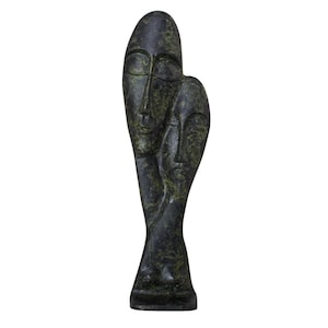 Op de afbeelding: Een donkergroene sculptuur die twee gestileerde gezichten afbeeldt, de ene boven de andere. De sculptuur heeft een gladde, gepolijste afwerking en een minimalistisch ontwerp. De gezichten hebben gesloten ogen en eenvoudige kenmerken, wat een gevoel van sereniteit creëert.