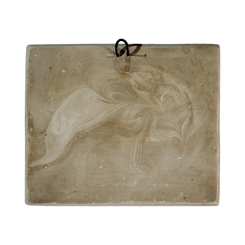 May include: A square, beige decorative tile with a swirled, marbled pattern in white. A black metal loop is attached to the top for hanging. The tile has a rustic, handmade appearance.