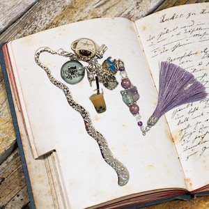 Può includere: Un segnalibro argentato con un designo decorativo e ciondoli, tra cui una tazza di caffè, una tazza di tè boba e un ciondolo con il testo "I Coffee Cats & Chill". Il segnalibro è attaccato a un fiocco viola.