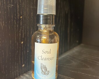 Puede incluir: Un frasco rociador de vidrio transparente con una tapa negra y una etiqueta que dice "Soul Cleanser". La etiqueta presenta manos rezando y un borde azul. La botella contiene un líquido marrón claro y se exhibe en un estante de madera oscura.