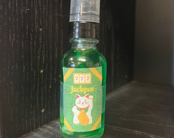 May include: A green glass bottle with a clear plastic cap. The label features the word "Jackpot" and a lucky cat illustration. The bottle is filled with a green liquid.